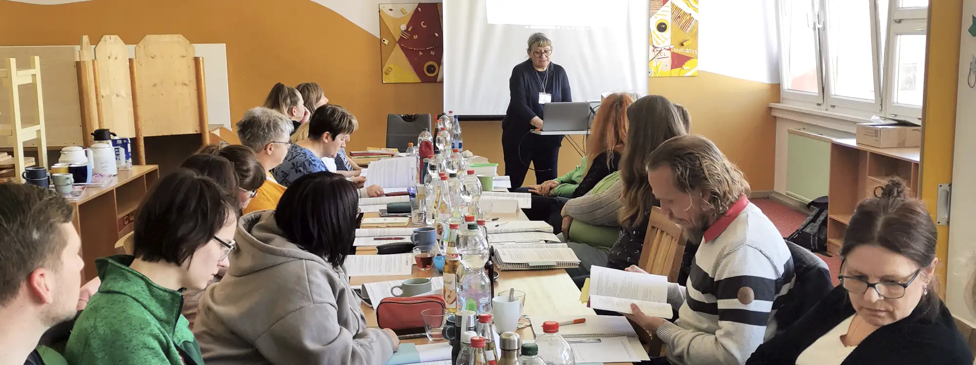 Kerstin Linaschk als Coach vor zuhörenden Teilnehmern, die an einem langen Tisch sitzen